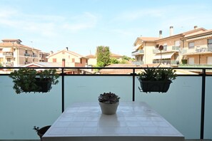 Un balcón con una mesa de baldosas, plantas en macetas y vistas a edificios residenciales.