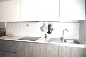 Cucina con mobili bianchi, lavello in acciaio inossidabile, piano cottura a induzione nero e utensili pensili.