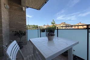 Un balcone con un tavolo bianco, due piante in vaso e una sedia bianca.