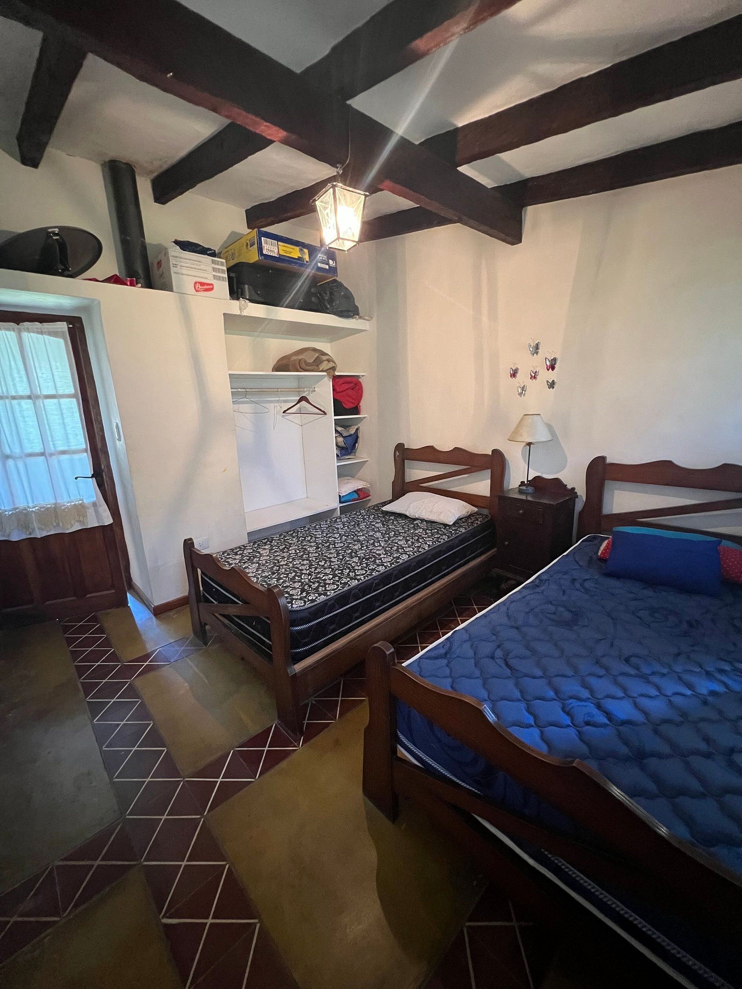 Ein Schlafzimmer mit zwei Betten, einem Kleiderschrank, einem Regal mit Gegenständen und einem Fenster mit Vorhängen.