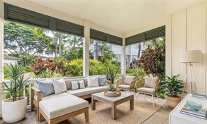 Un salón amplio con sofá, sillas, una mesa de centro y ventanas grandes con vistas a un jardín.