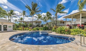 A swimming pool with a hot tub, surrounded by palm trees and a building with a balcony.