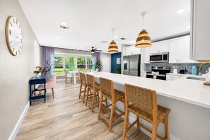 A modern kitchen with a central island, wooden chairs, and pendant lighting. - Salty Flamingo | Heated Pool & Spa Near Beaches (Seminole)