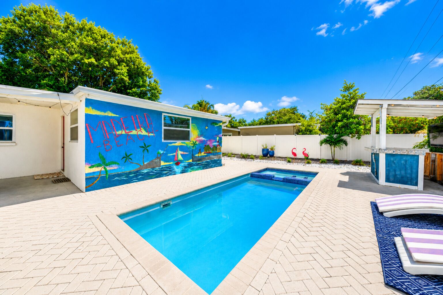 A swimming pool with a mural, a covered seating area, and a fenced backyard.