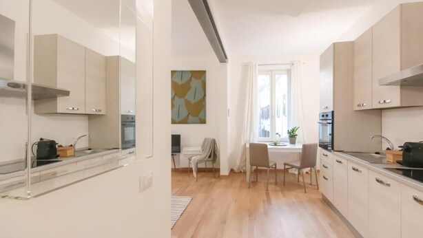 Una cocina moderna con armarios de madera clara, un comedor con mesa y sillas, y un ventanal con cortinas.