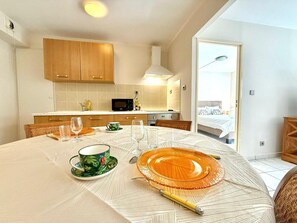 A modern kitchen with wooden cabinets, a microwave, and a dining area with a table set for two. - La Métiss, City Center and Private Parking (Saint-Denis)