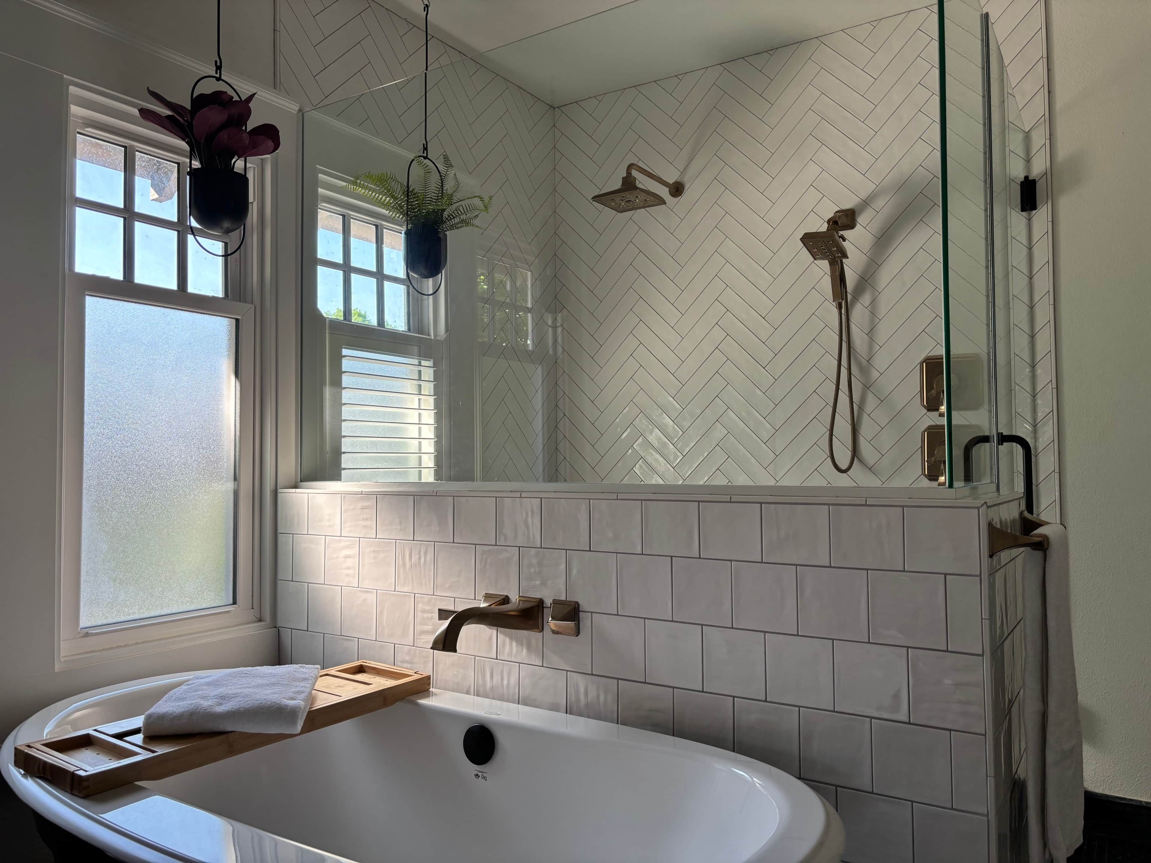 A bathroom with a freestanding bathtub, a window with blinds, a shower with a glass enclosure, and a potted plant.