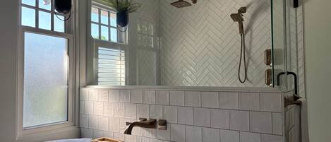 A bathroom with a freestanding bathtub, a window with blinds, a shower with a glass enclosure, and a potted plant.