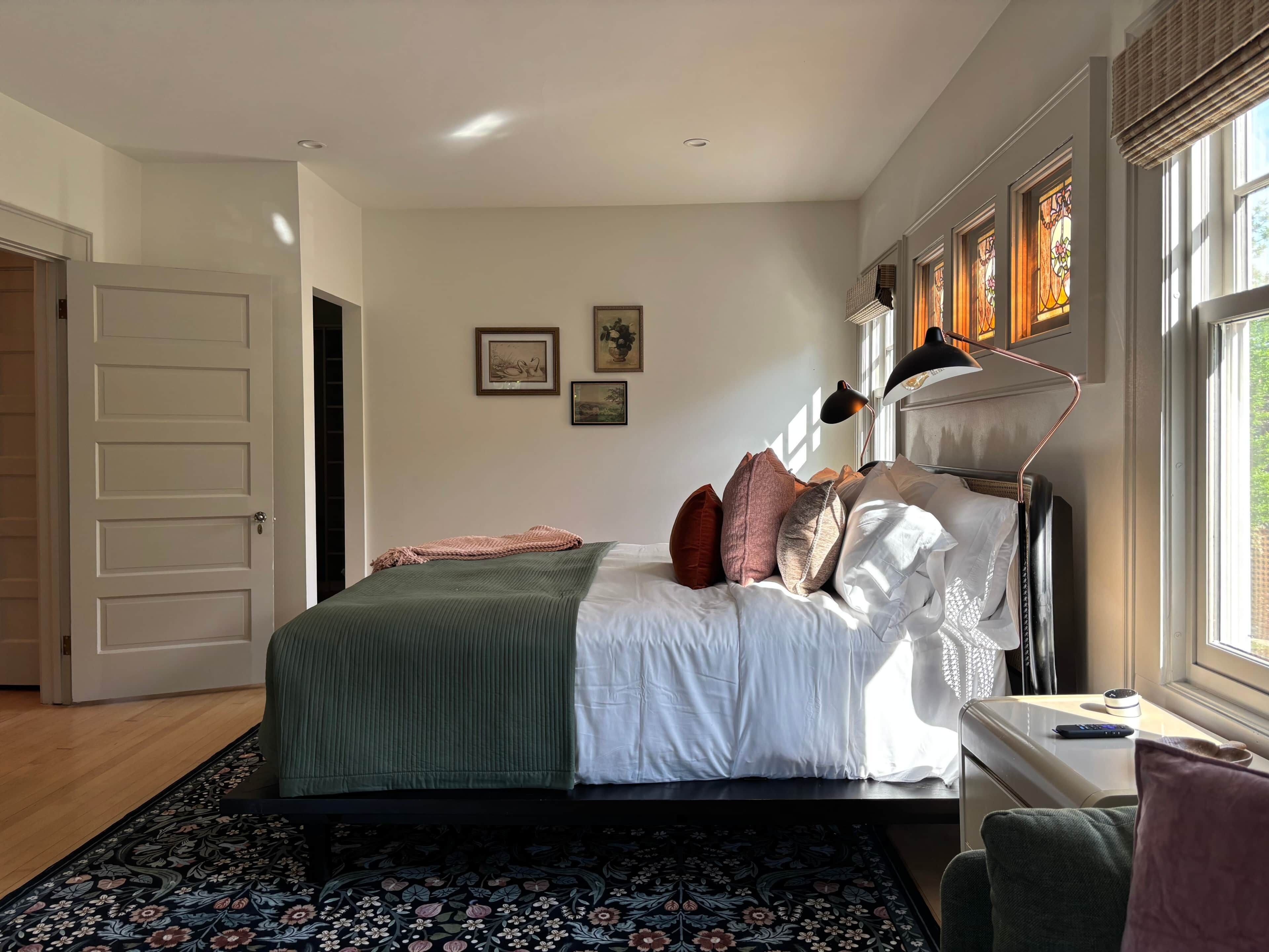A bedroom with a bed, bedside table, lamp, and a window with a view.