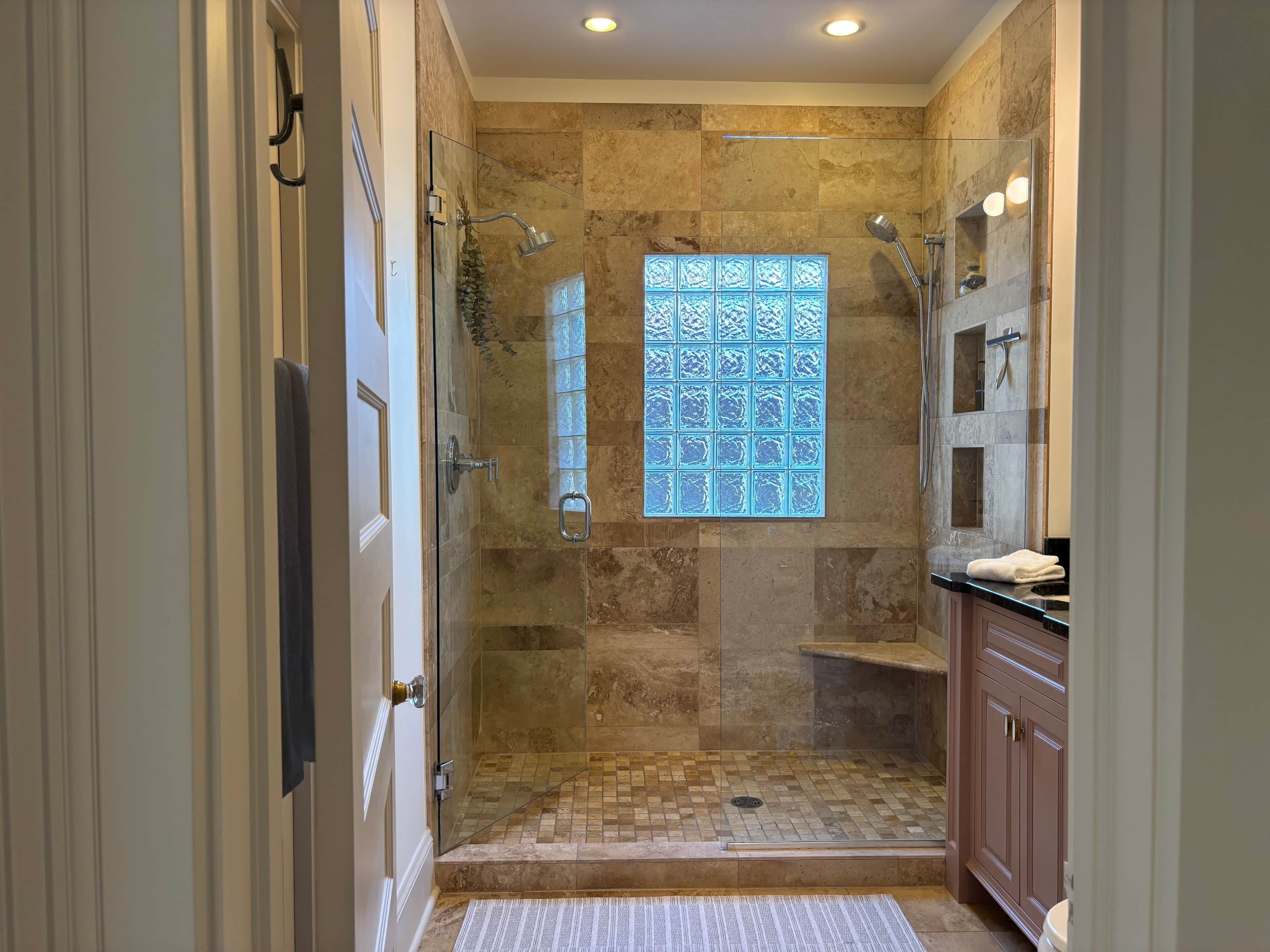 A walk-in shower with a glass door, a window with a geometric pattern, and a tiled floor.