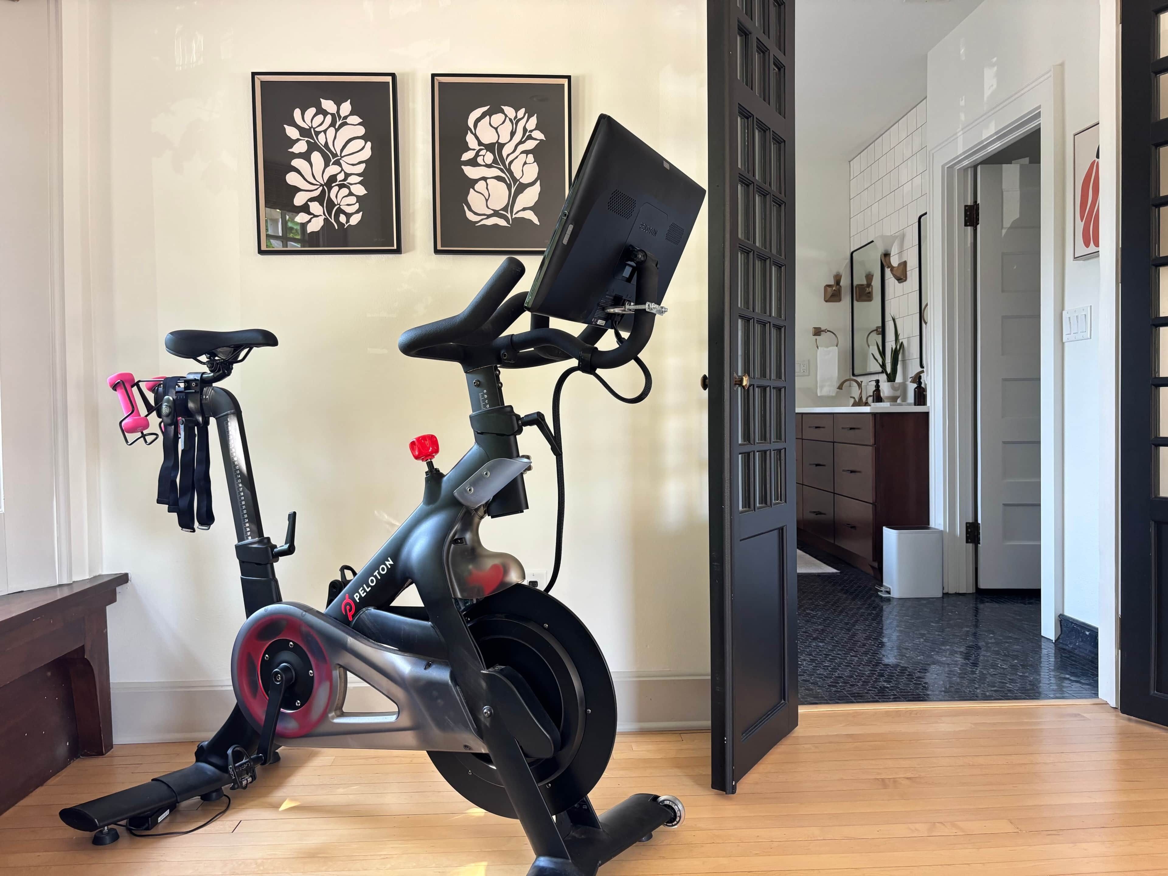 A stationary bike in a room with a wooden floor, a bench, and a door leading to a bathroom.