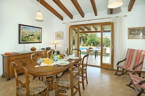 A dining area with a wooden table, chairs, and a view of the outdoors. - Villa Almedra Boi in Pollensa for 2 with Garden, Pool, Wi-Fi & A/C (Pollença)