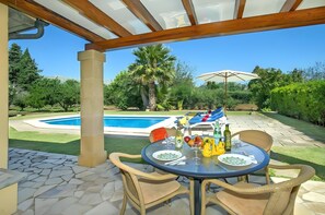 An outdoor patio with a table set for dining, a pool, and lush greenery in the background. - Villa Almedra Boi in Pollensa for 2 with Garden, Pool, Wi-Fi & A/C (Pollença)