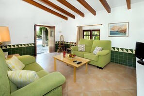 A living room with green sofas, a wooden coffee table, and a painting on the wall. - Villa Almedra Boi in Pollensa for 2 with Garden, Pool, Wi-Fi & A/C (Pollença)