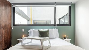 Un dormitorio con cama, mesitas de noche, ventana con persianas y vista al exterior.