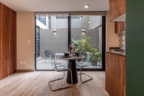 Una cocina moderna con una mesa redonda, dos sillas, una planta en maceta y vistas a un espacio exterior con pared de ladrillo y una escalera.