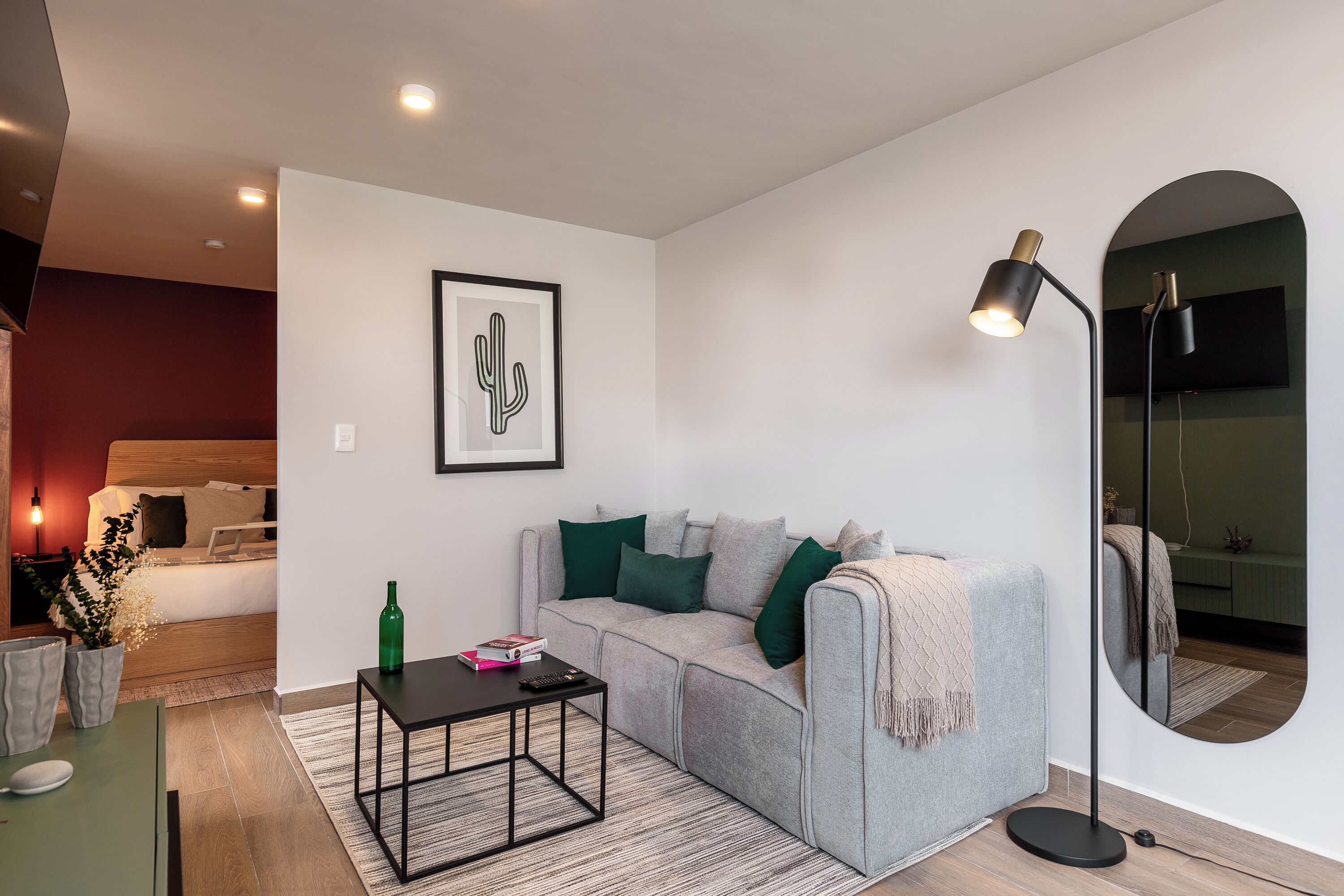 Una sala de estar moderna con un sofá gris, una mesa de centro, una lámpara de pie, una obra de arte con forma de cactus enmarcada y un espejo.