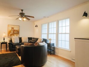 Ein Wohnzimmer mit einer schwarzen Ledersofa, einem runden Hocker, einem Deckenventilator und großen Fenstern.