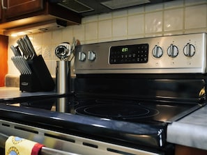 Une cuisine équipée d’une cuisinière, d’une horloge numérique et d’un ensemble de couteaux.