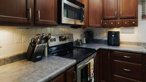 Una cocina con armarios de madera, microondas de acero inoxidable, estufa y cafetera.
