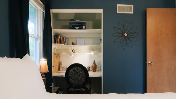 Un dormitorio con cama, escritorio, silla, estantería y puerta.