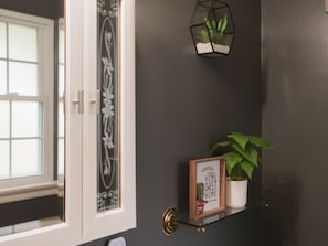 Un mur sombre orné d’une porte décorative, une petite plante en pot et un panneau encadré.