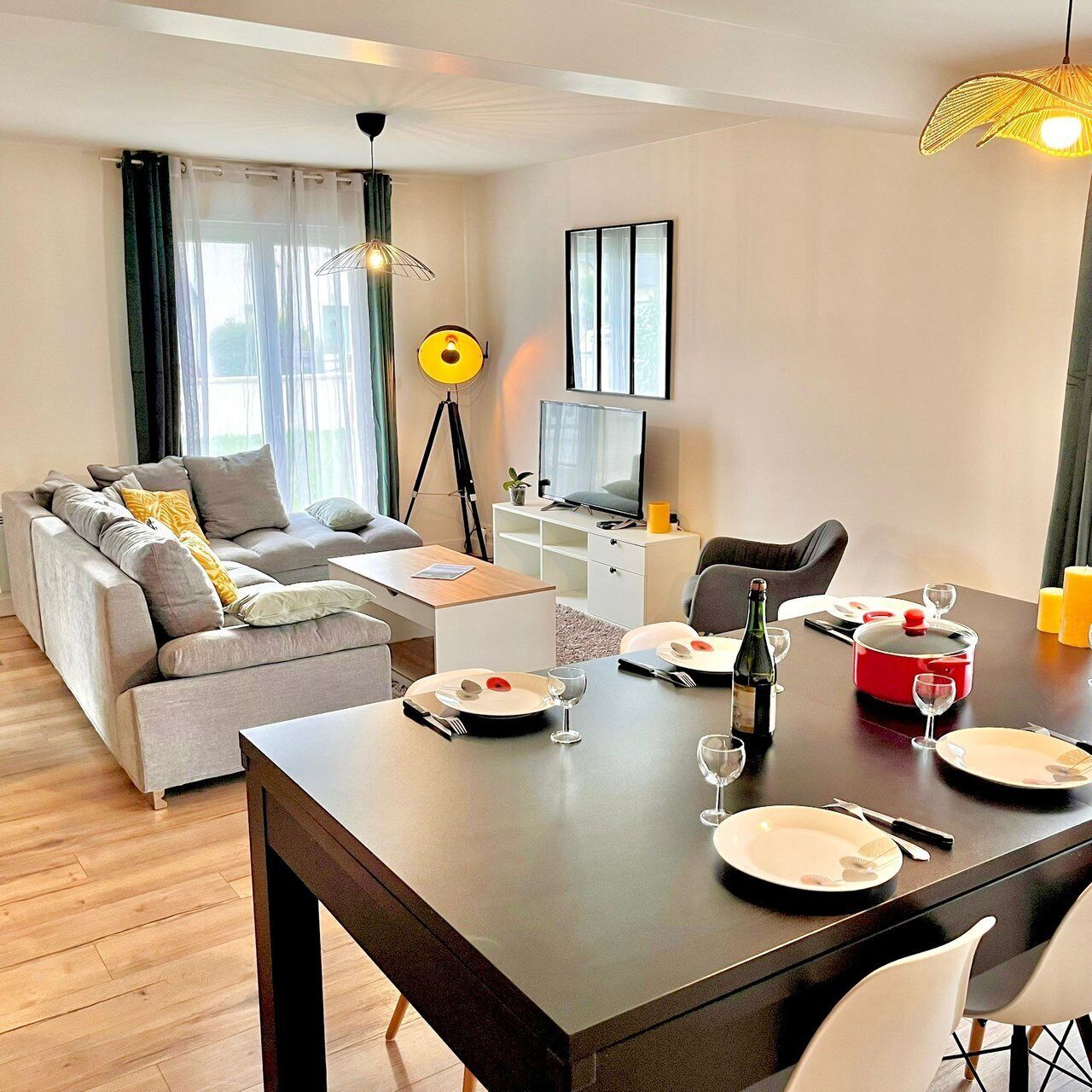 A modern living room with a sofa, dining table set for two, a TV, and a lamp.