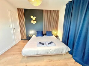 Una habitación de hotel moderna con una cama grande, un adorno de Mickey Mouse montado en la pared, una lámpara de noche y una cortina.