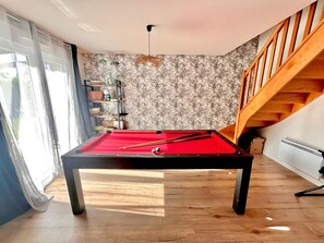 Una mesa de billar en una habitación con una escalera de madera, un radiador y un papel tapiz estampado.