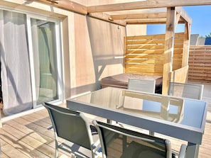 Un patio al aire libre con una mesa y sillas de vidrio, una pérgola de madera y una puerta corrediza de vidrio.