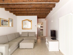 Ein Wohnzimmer mit einer Couch, einem Hocker, einem Fernseher und einem weißen Schrank.