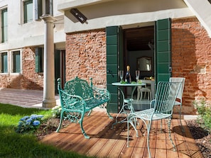 Eine Terrasse mit Tisch und zwei Stühlen, einer Weinflasche und einem Glas.