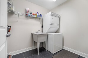 A compact laundry room with a washing machine, a sink, and a shelf with cleaning supplies.