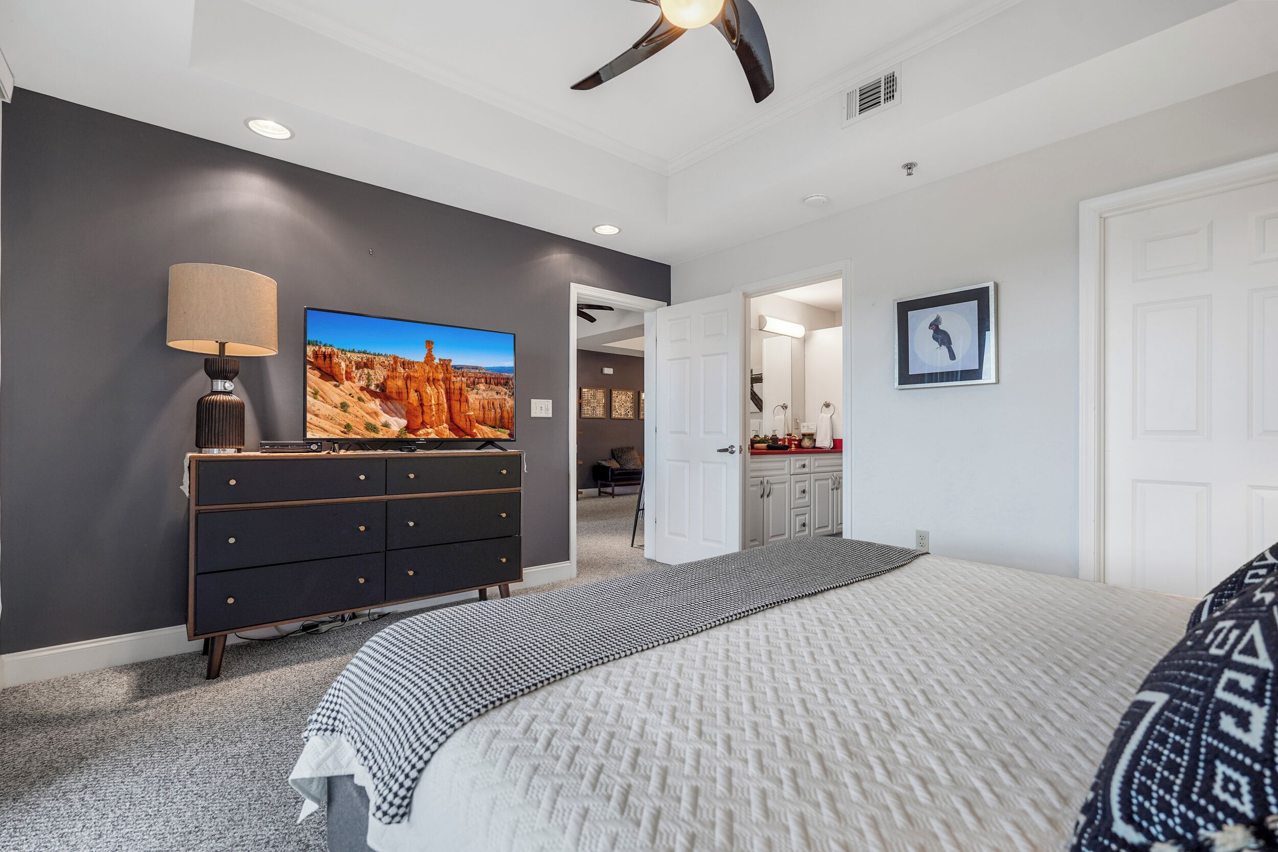 A bedroom with a bed, a dresser, a television, and a ceiling fan.