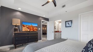 Une chambre à coucher avec un lit, une commode, un téléviseur et un ventilateur de plafond.