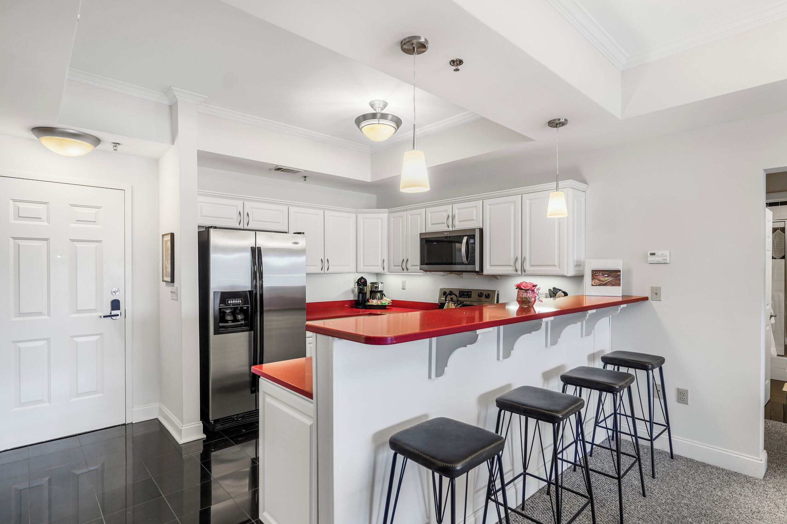 A modern kitchen with white cabinetry, a stainless steel refrigerator, a microwave, and a red island with bar stools.