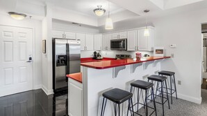 Une cuisine moderne avec des meubles blancs, un réfrigérateur en acier inoxydable, un four à micro-ondes et un îlot central rouge agrémenté de tabourets de bar.