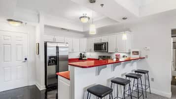A modern kitchen with white cabinetry, a stainless steel refrigerator, a microwave, and a red island with bar stools.