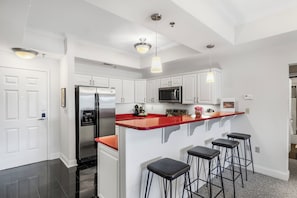 Eine moderne Küche mit weißen Schränken, einem Edelstahl-Kühlschrank, einer Mikrowelle und einer roten Kochinsel mit Barhocker.
