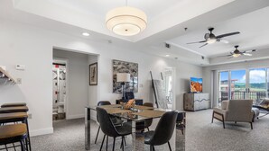 Un vaste espace de vie comprenant une table à manger avec un plateau en verre, des chaises noires, un canapé et un ventilateur de plafond.