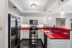 A modern kitchen with stainless steel appliances, white cabinetry, and a red countertop.
