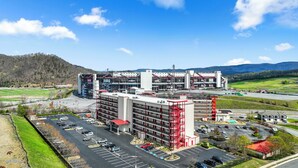 Un parking à plusieurs étages, avec un bâtiment rouge et blanc au premier plan, un grand stade en arrière-plan et un paysage montagneux.