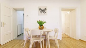 Ruokailutila, jossa on pyöreä pöytä ja neljä tuolia, maljakko kukkineen sekä seinälle ripustettu taideteos.