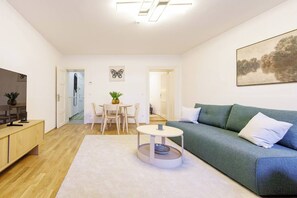 A modern living room with a sofa, a coffee table, a dining area with chairs, and a TV on a cabinet. - Prime Vienna Location - Sleeps 5 (Vienna)