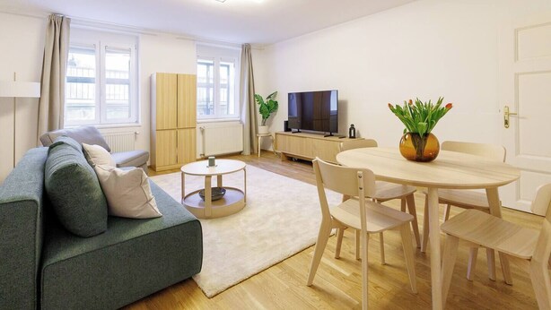 Moderni olohuone, jossa on sohva, ruokapöytä tuoleineen, televisio ja ruukkukasvi.
