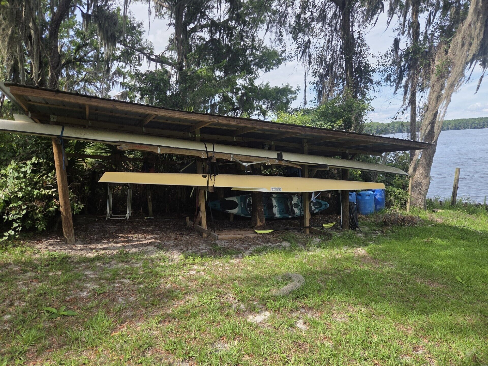 A covered outdoor area with a roof, surrounded by trees and a body of water.