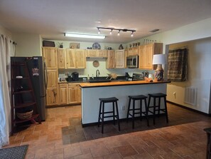 Eine Küche mit Holzschränken, einem Kühlschrank, einer Mikrowelle, einem Herd und einer Bar mit Hockern.