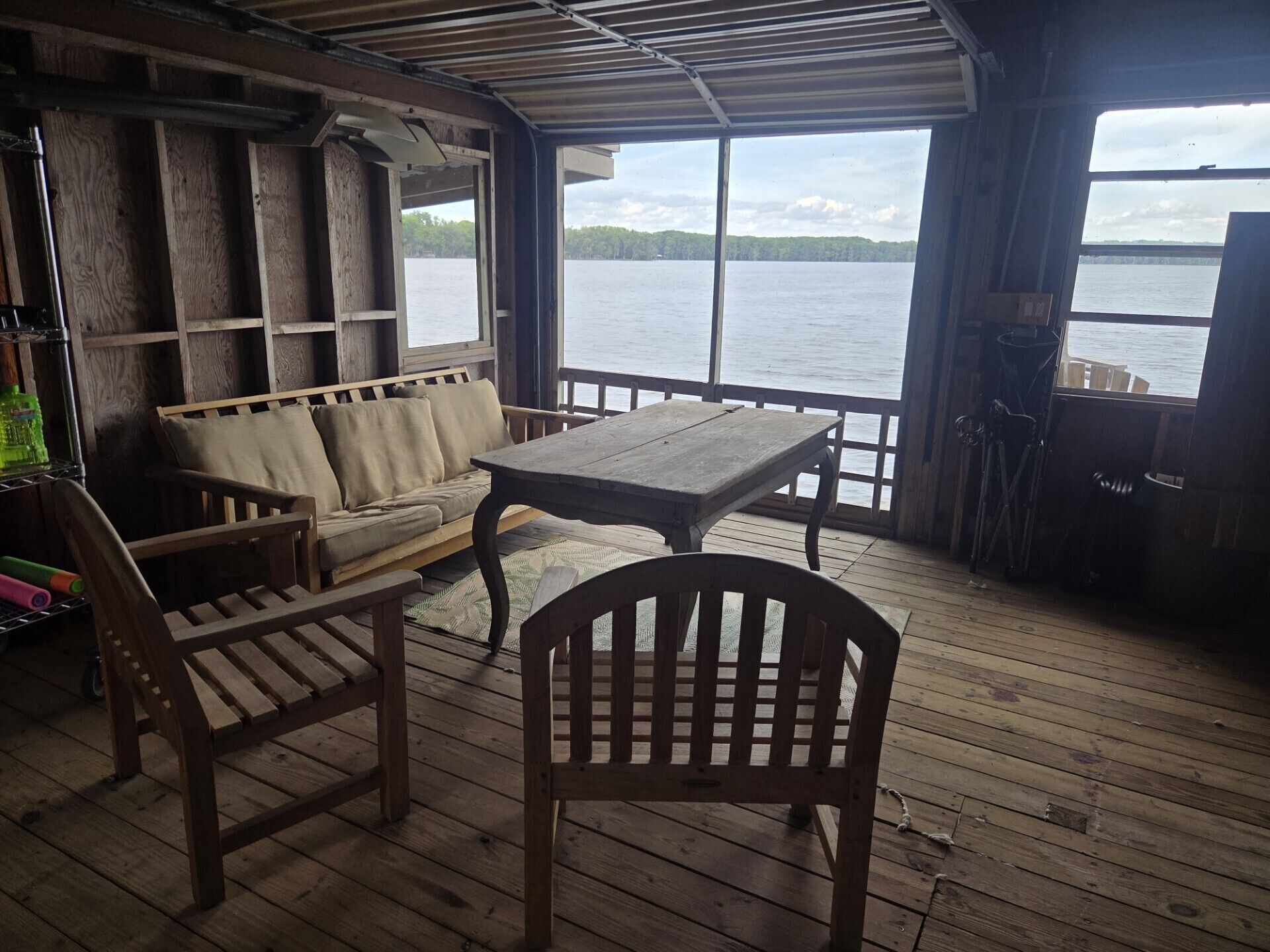 A wooden deck with a table and chairs, a sofa, and a view of a lake.
