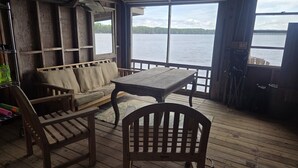 Um deck de madeira com mesa e cadeiras, um sofá e vista para um lago.