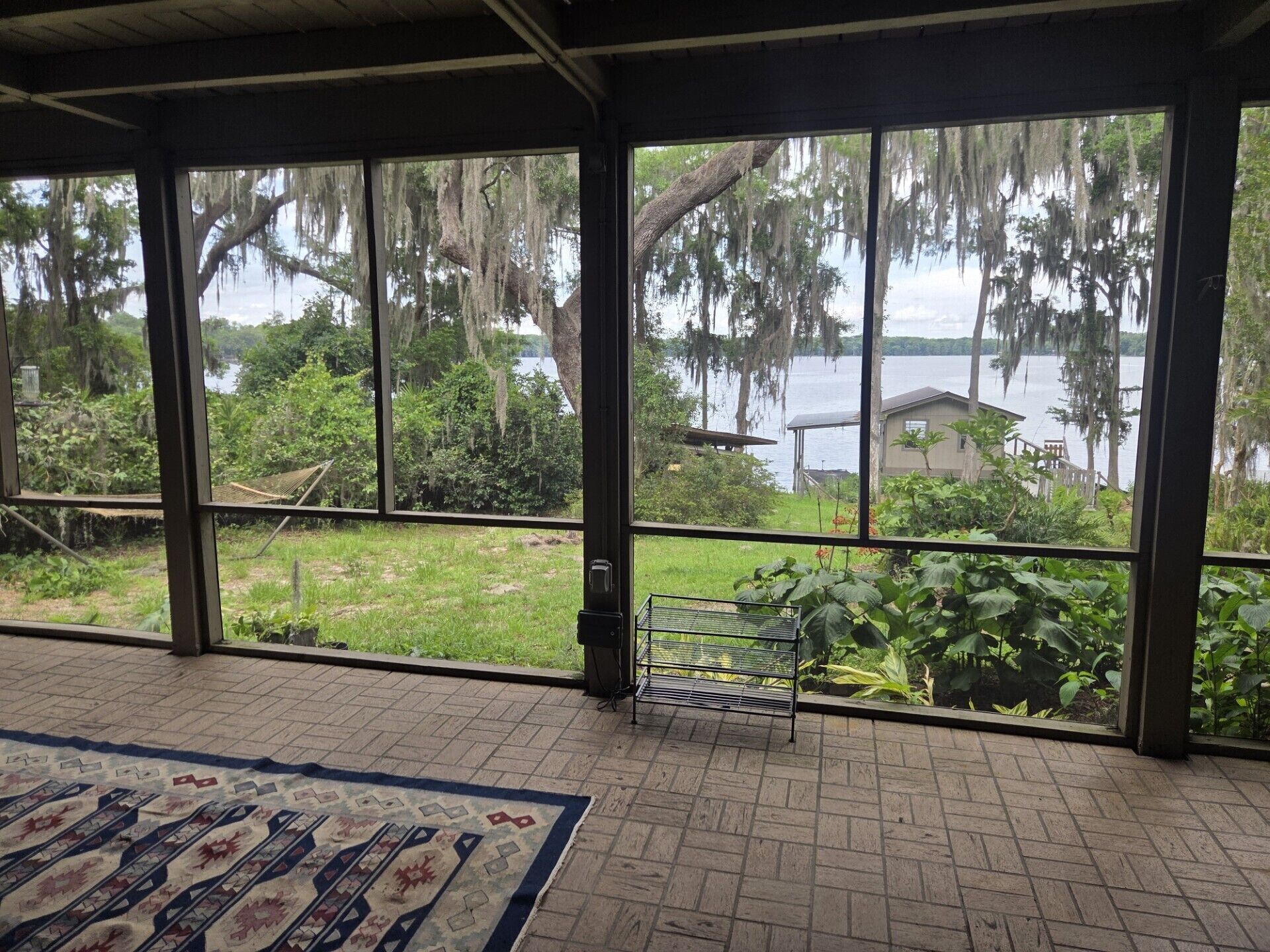 A room with large windows overlooking a lake, a patterned rug, and a metal rack.